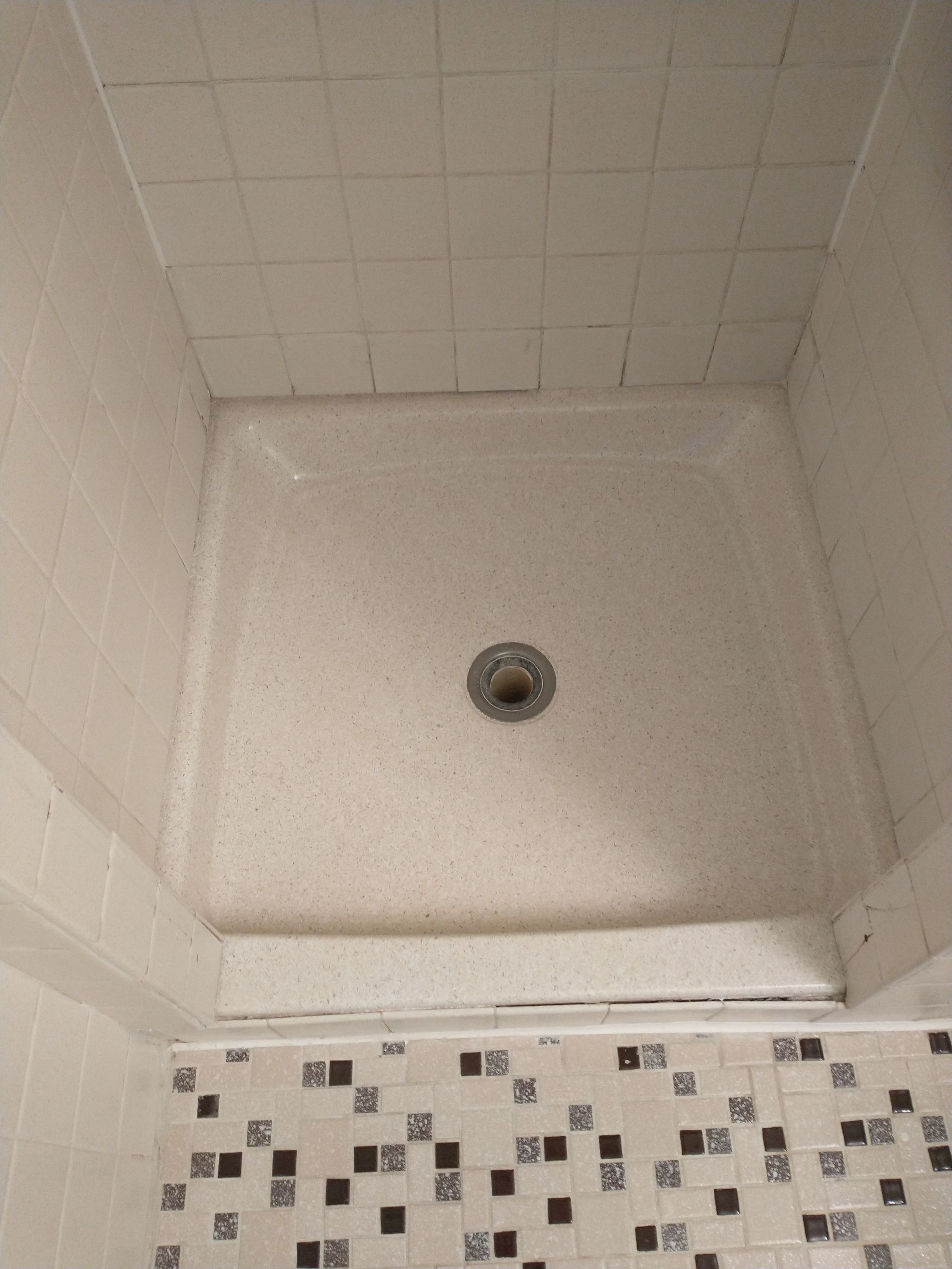 Shower stall with a white speckled base and tiled walls.