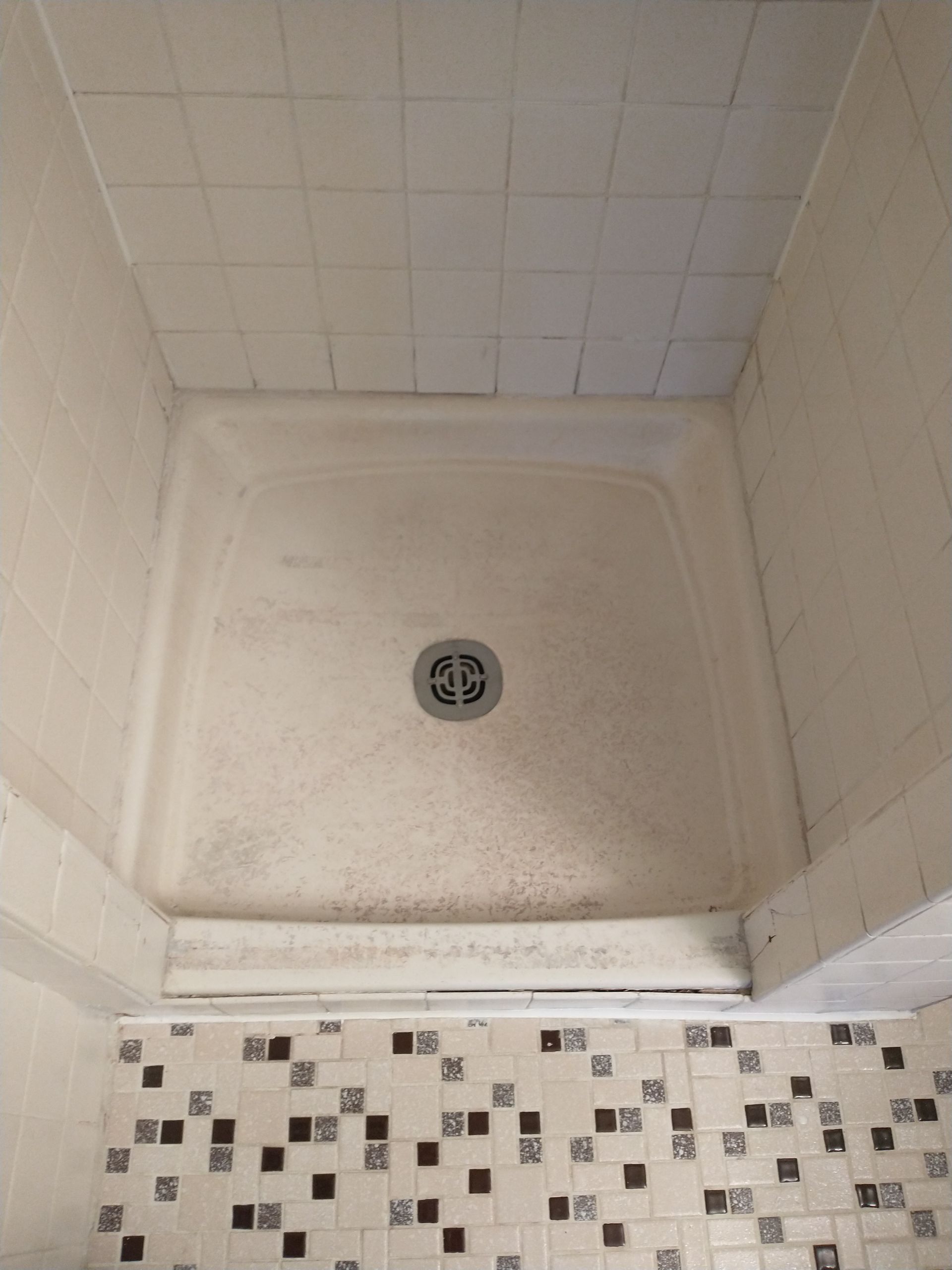 Shower stall with white tiled walls, a light-colored base, and a drain.