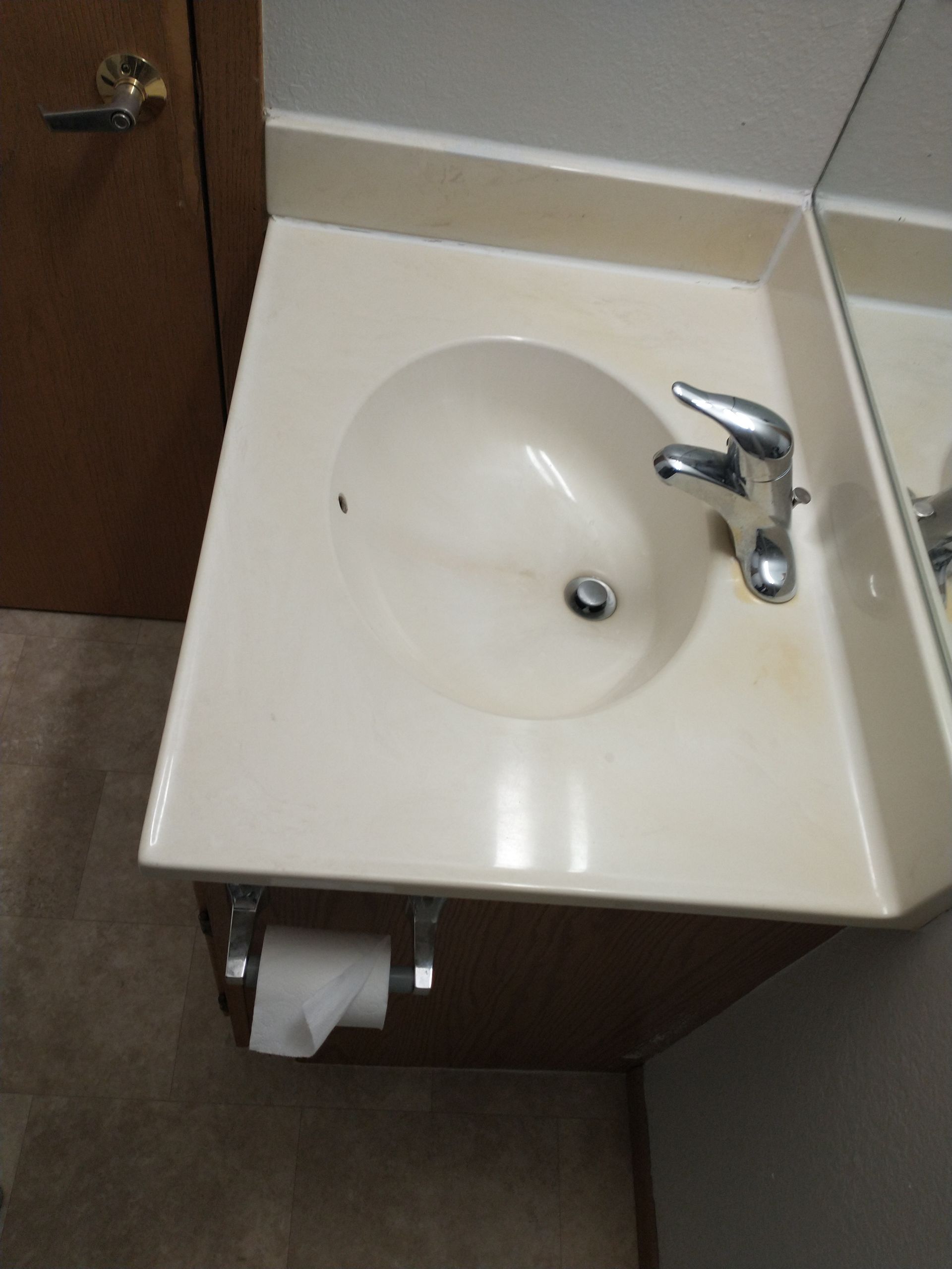 Beige bathroom sink with a chrome faucet. Cabinet below with toilet paper roll.