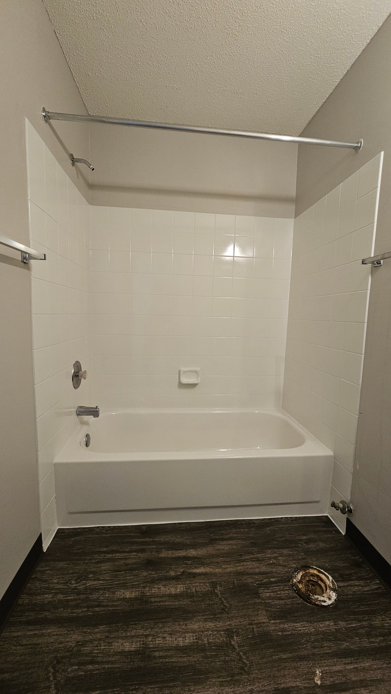 White tiled shower/tub with a curved shower rod. Dark flooring and gray walls.