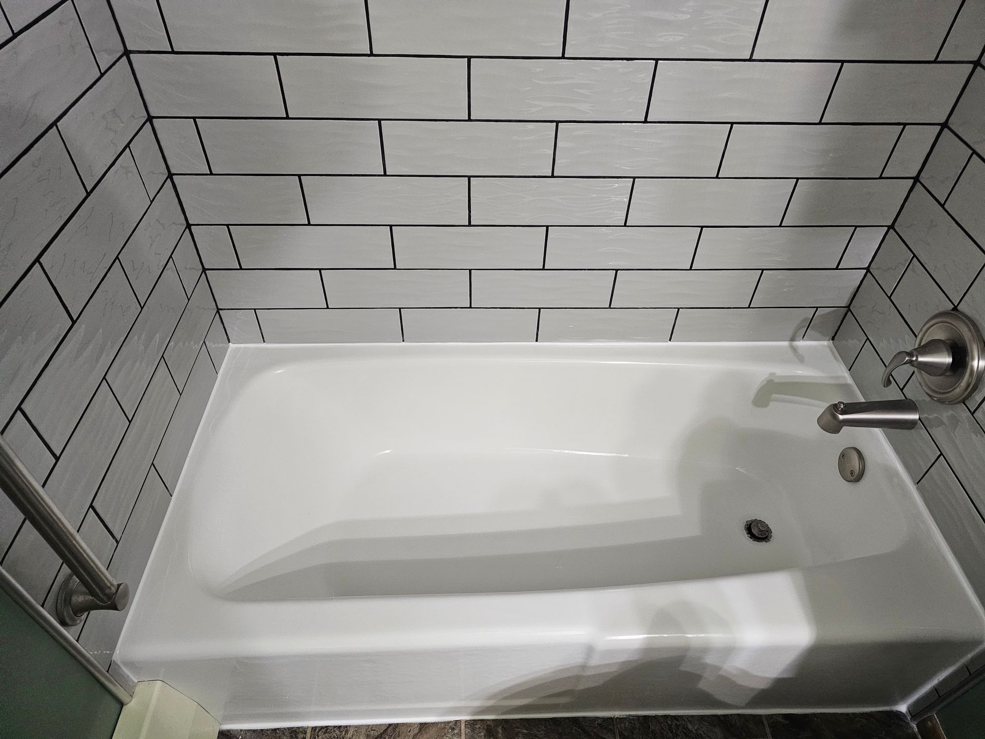 White bathtub in a tiled shower enclosure, with faucet and grab bar.