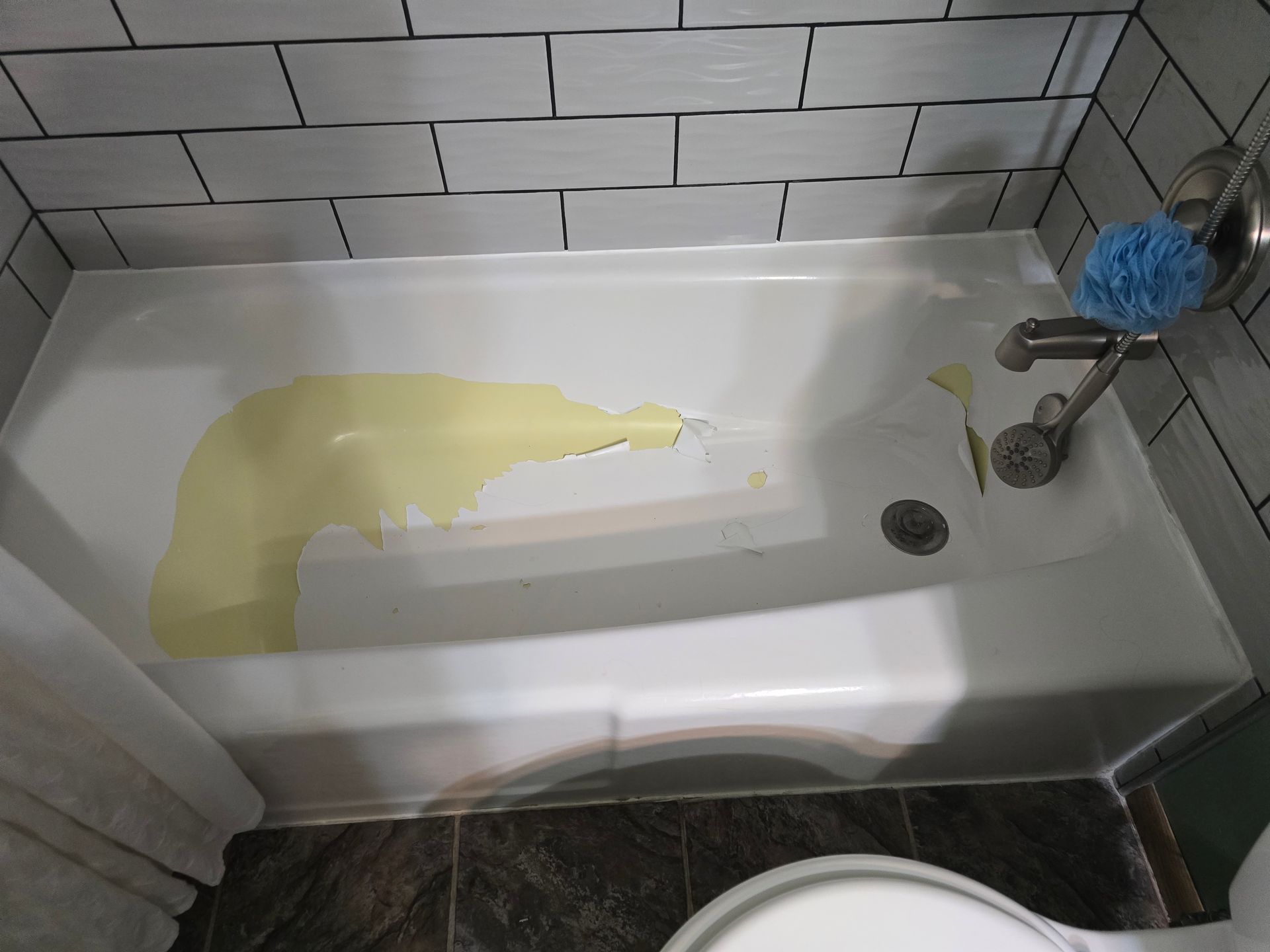 Yellow liquid covering the inside of a white bathtub, against a backdrop of white and dark gray tiles.