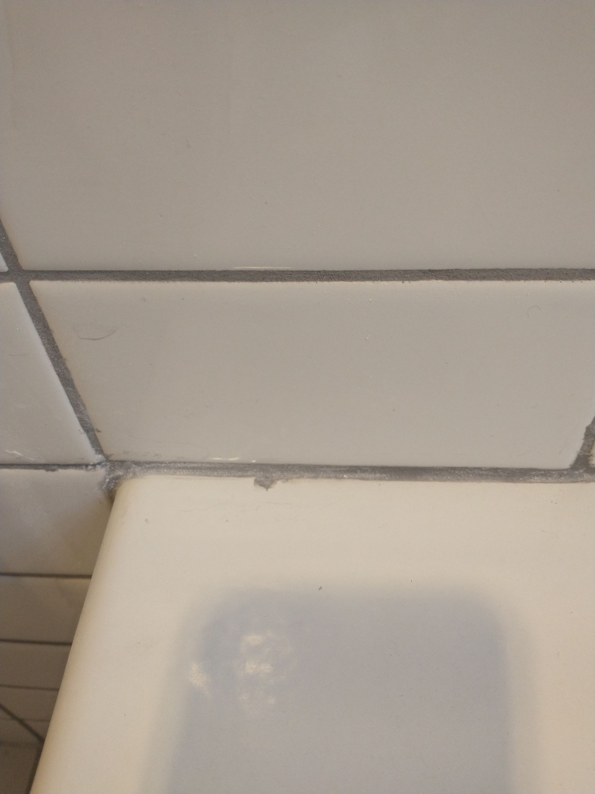 White tiled bathroom wall and tub, with gray grout lines.