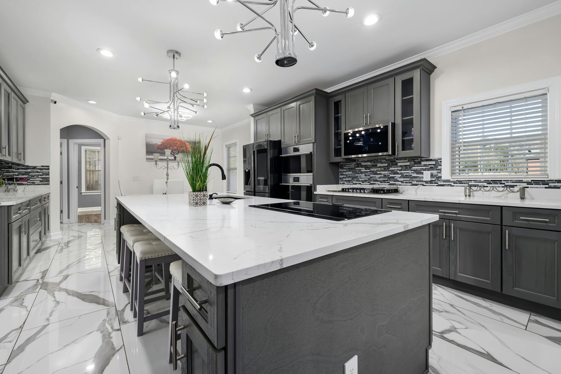 Gray kitchen with large island, marble floors, and modern light fixtures.