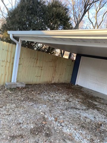 A carport with a wooden fence behind it and a white garage door.