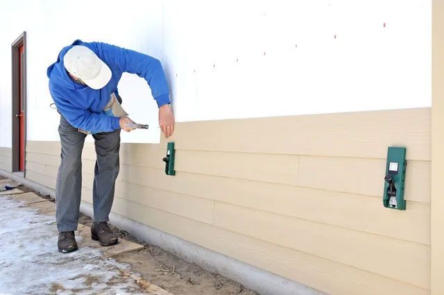 A man installing fibrous cement siding using siding gauges