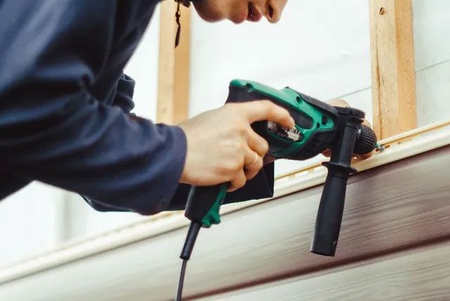 A man skilfully uses a drill for new home siding installation in Champaign & Springfield, IL, enhancing property aesthetics. A man skilfully uses a drill for new home siding installation in Champaign & Springfield, IL, enhancing property aesthetics.
