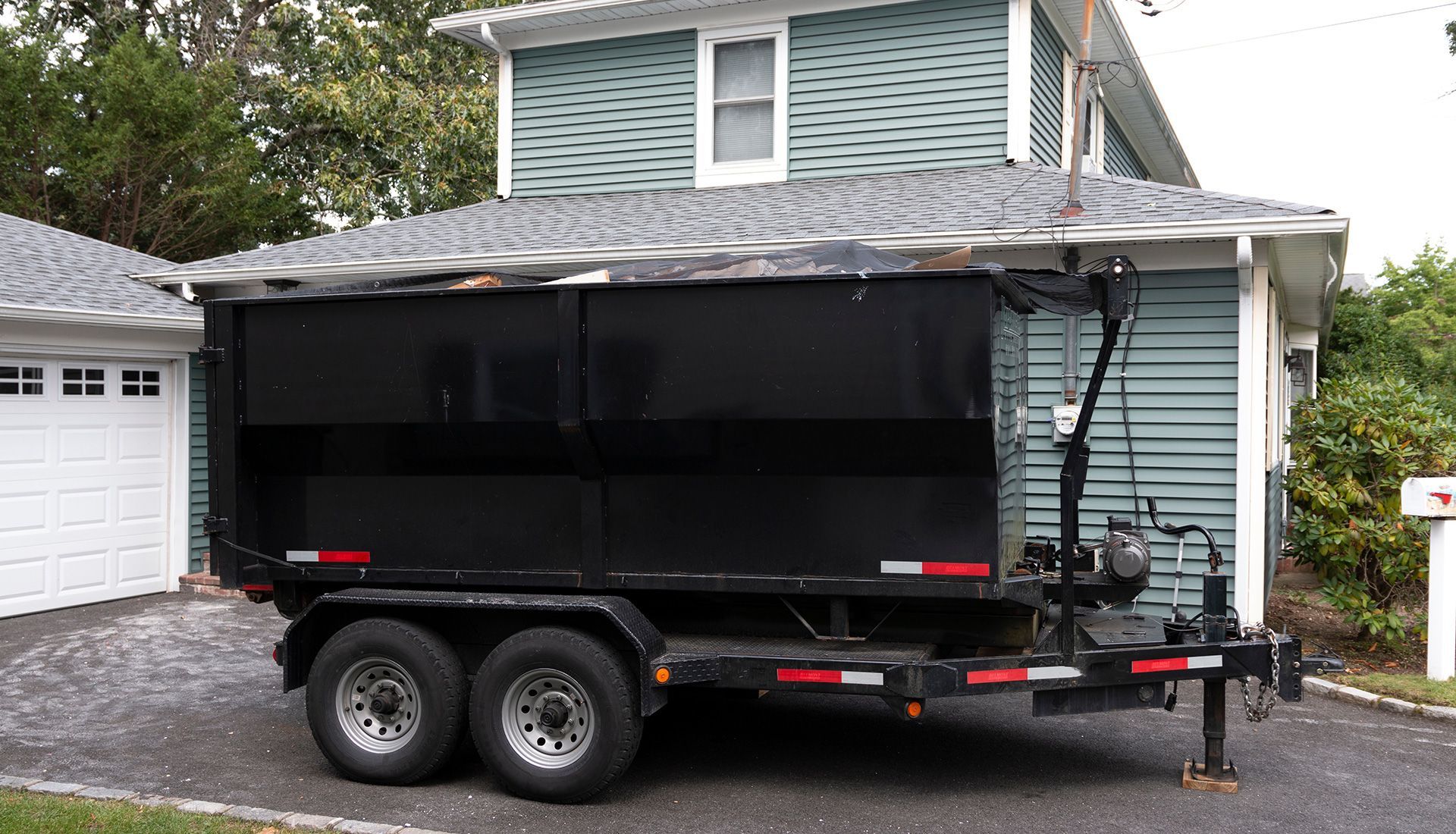 Garbage truck worker loading a yellow bin into a green truck on a road.