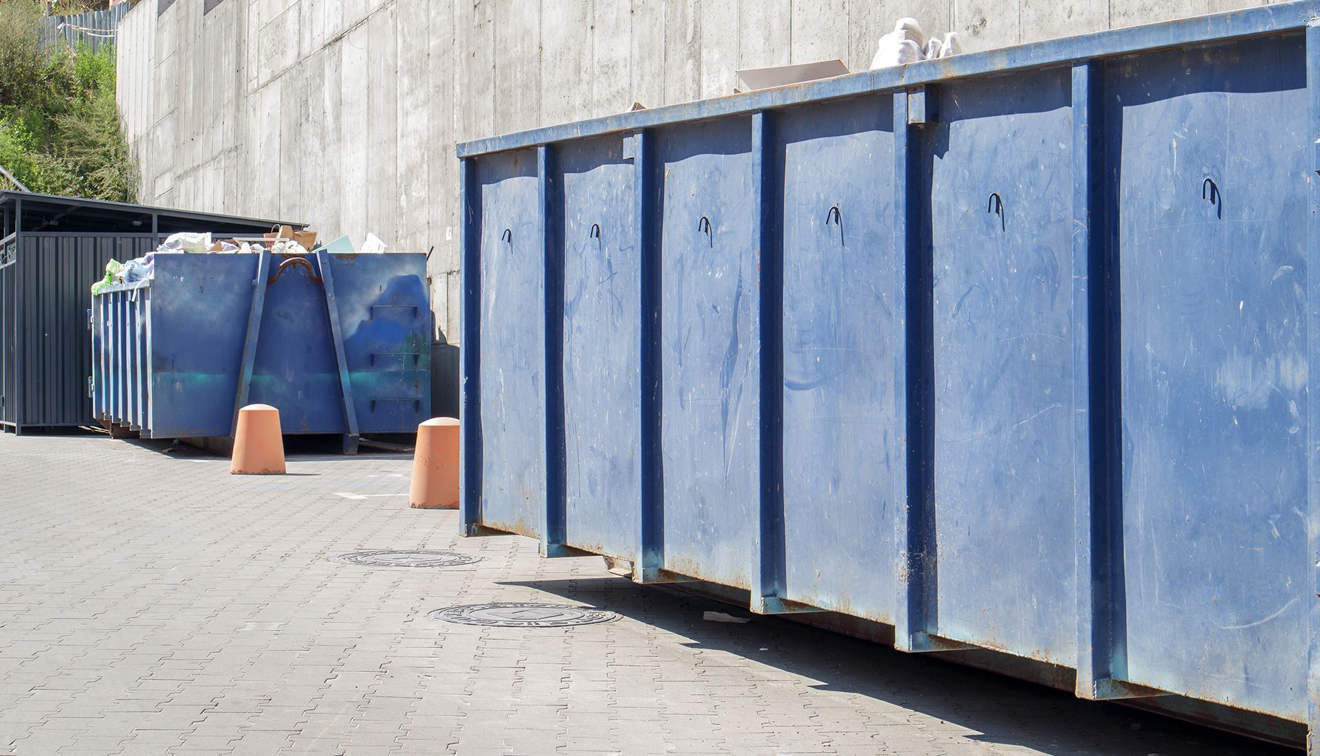 Blue metal dumpsters lined up against a concrete wall.