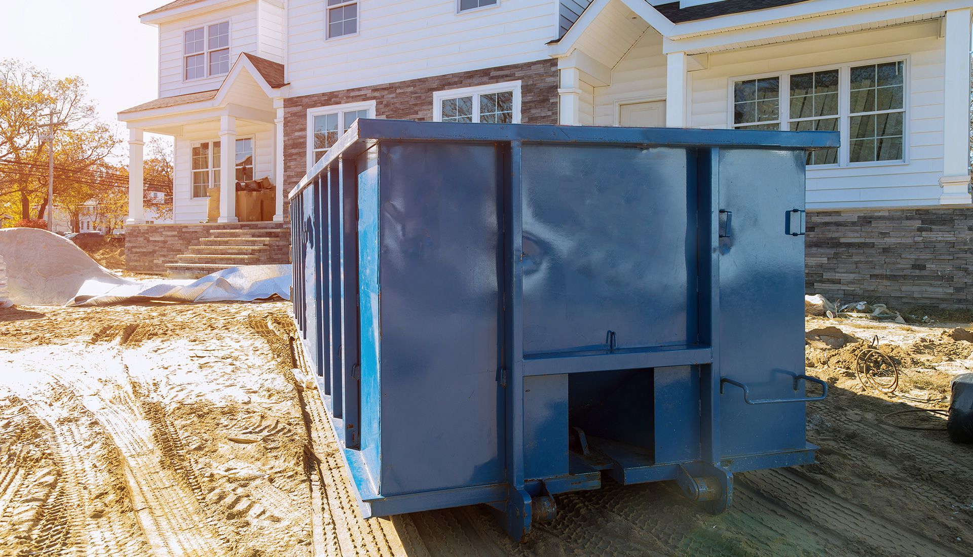 Blue dumpster in front of a house under construction; a construction site.