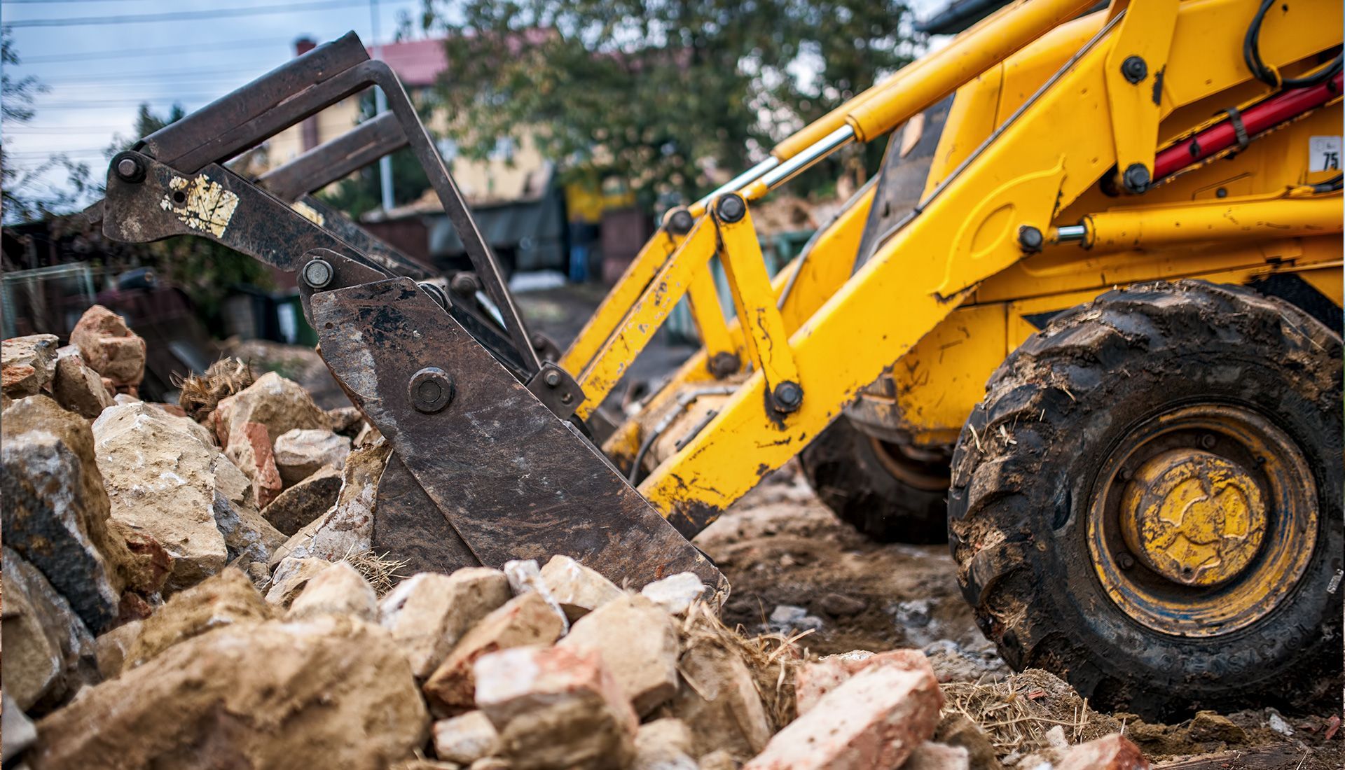 Yellow backhoe lifting a pile of bricks at a construction site.
