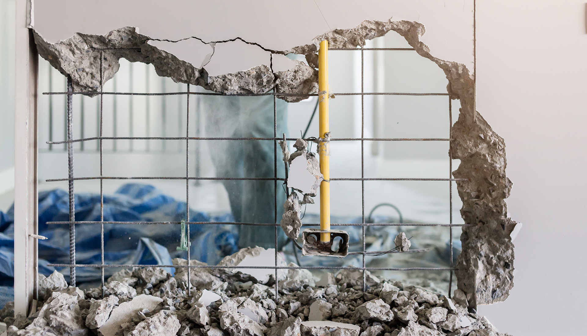 Excavator demolishing a red-tiled roof with its claw, exterior shot, blue sky.
