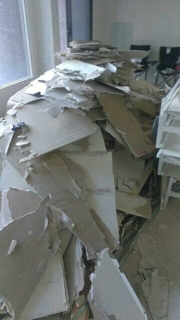 Pile of torn drywall debris in a room with a window and shelving.