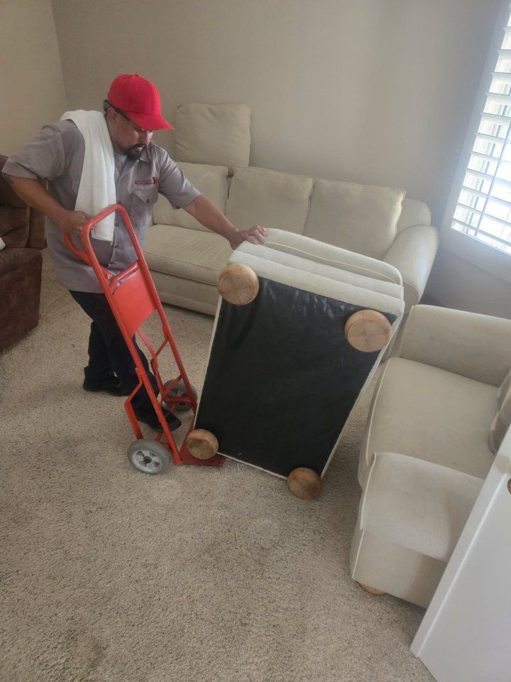 Person using a hand truck to move a white chair in a living room.
