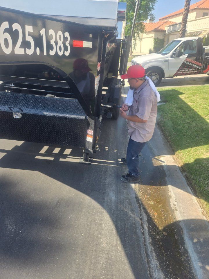 Man next to a black trailer, holding a phone, on a paved road. White pickup truck visible in the background.
