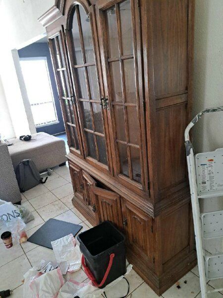 Wooden display cabinet with glass doors. Room has a chair and debris on the floor.