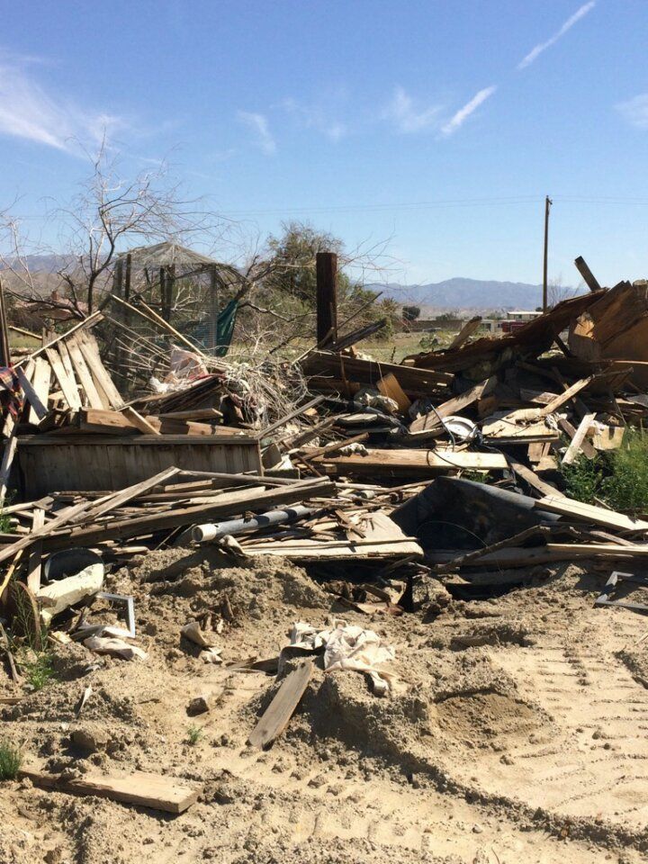 Debris of a destroyed structure on a dirt lot, with a distant mountain range under a blue sky.