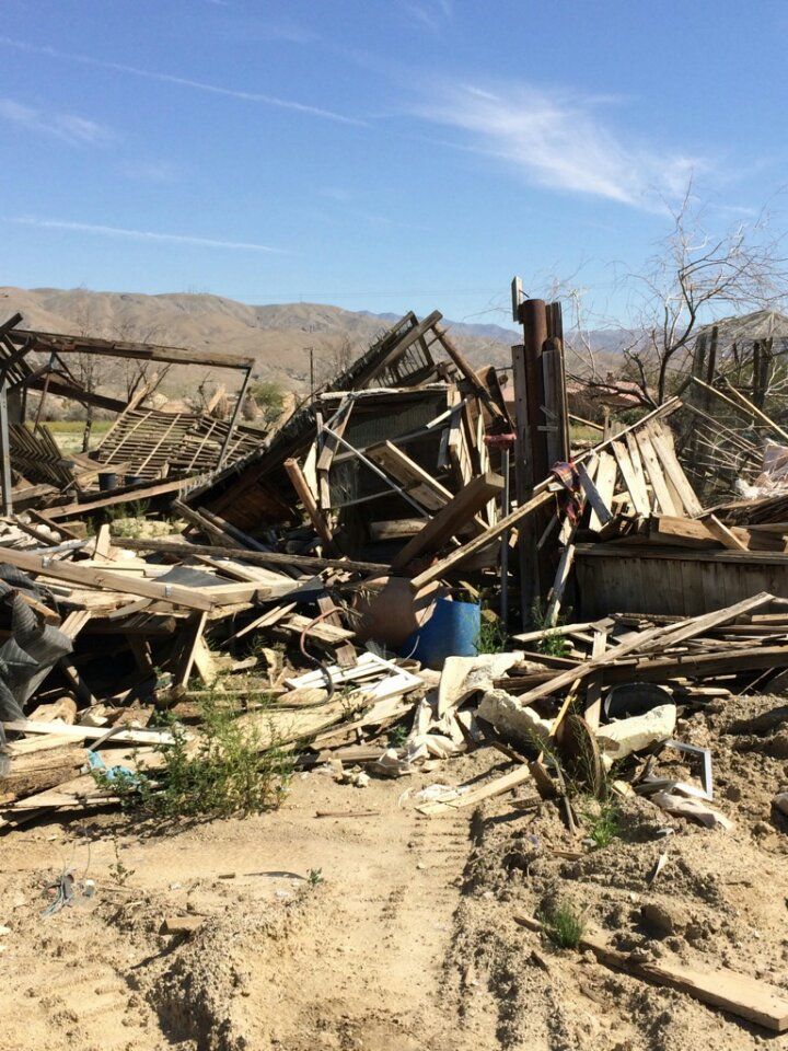 Debris of a collapsed wooden building, against a desert backdrop.