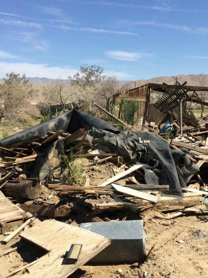 Debris and collapsed wooden structure, possibly a building, in a desert landscape under a blue sky.