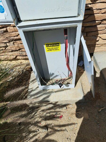 Open electrical box with exposed wires, yellow caution sign, and door ajar.