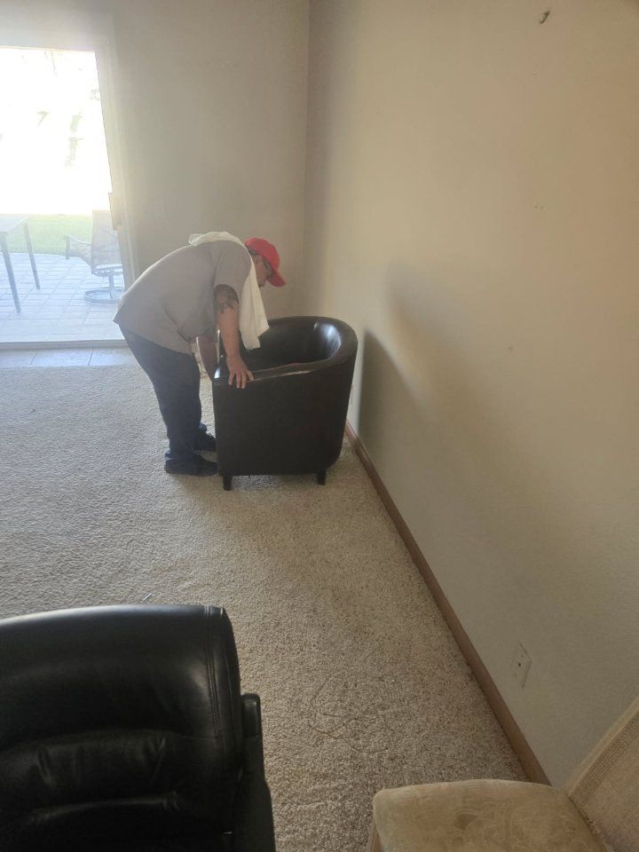 Person leaning over a dark chair in a room with light carpet and a sliding glass door.