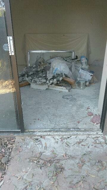 Open sliding glass door reveals debris and a mattress inside a concrete room.