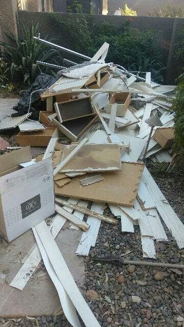 Pile of construction debris on a gravel path, including wood pieces, a box, and metal.