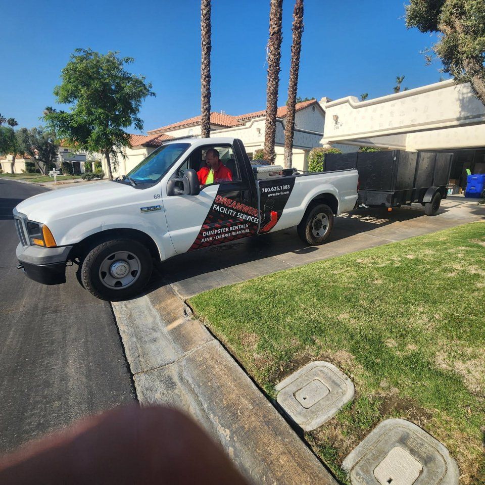 White pickup truck with trailer on residential street, palm trees in background.