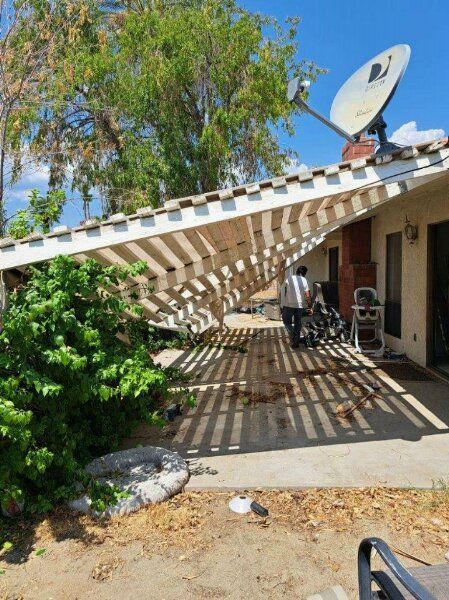 Damaged patio cover, leaning towards the ground. A person is near the collapsed structure. Satellite dish on the roof.