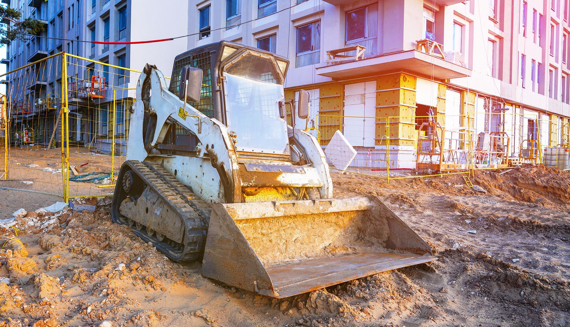 Skid steer loader on a construction site, scooping dirt in front of a building.