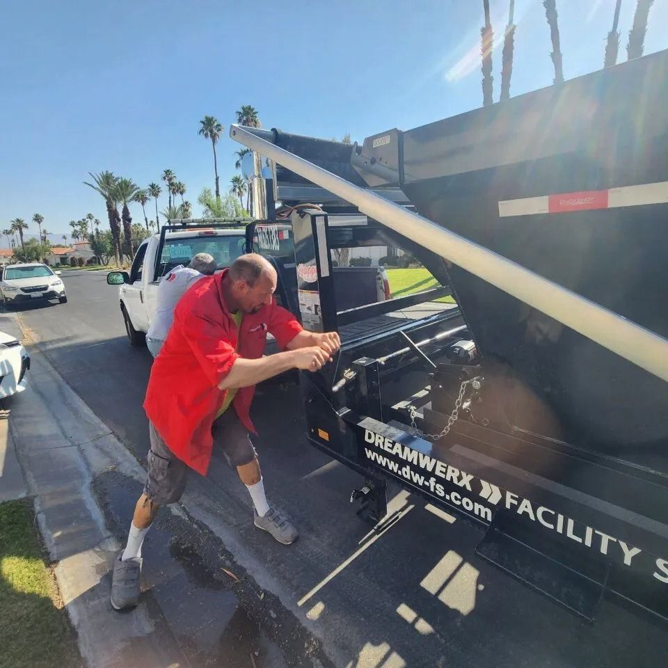 Man in red shirt operating a dump truck in a sunny outdoor setting.