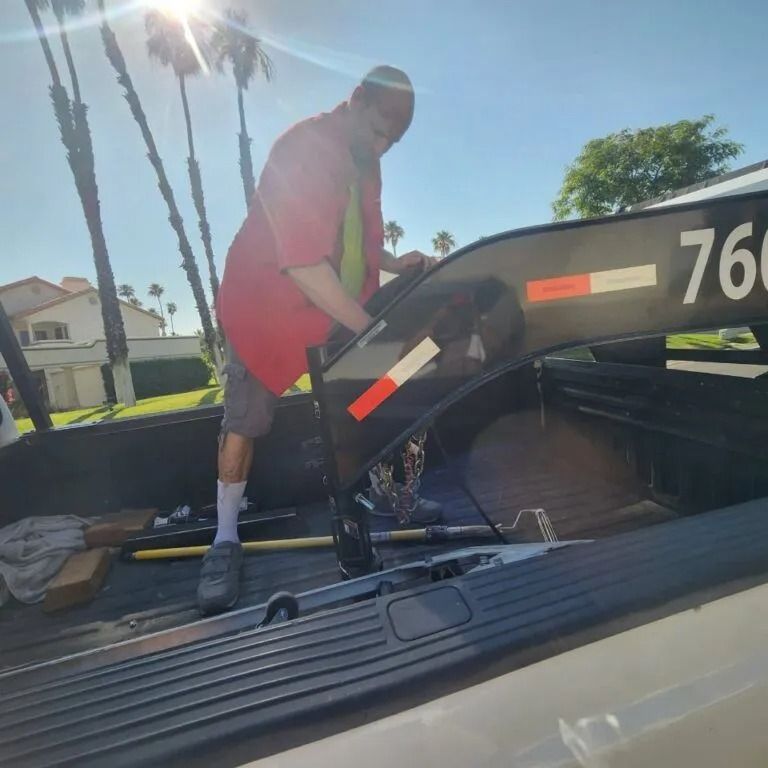 Person in red shirt adjusting a trailer hitch in a truck bed on a sunny day.
