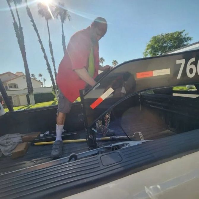 Person in red shirt adjusting a trailer hitch in a truck bed on a sunny day.