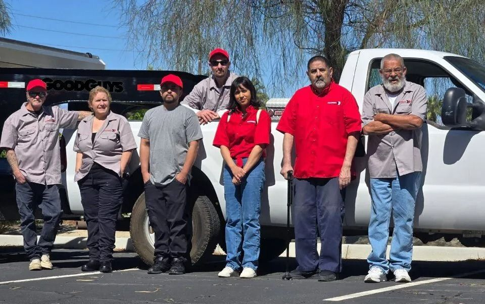 Group of people in work uniforms posing in front of a white truck on a sunny day.