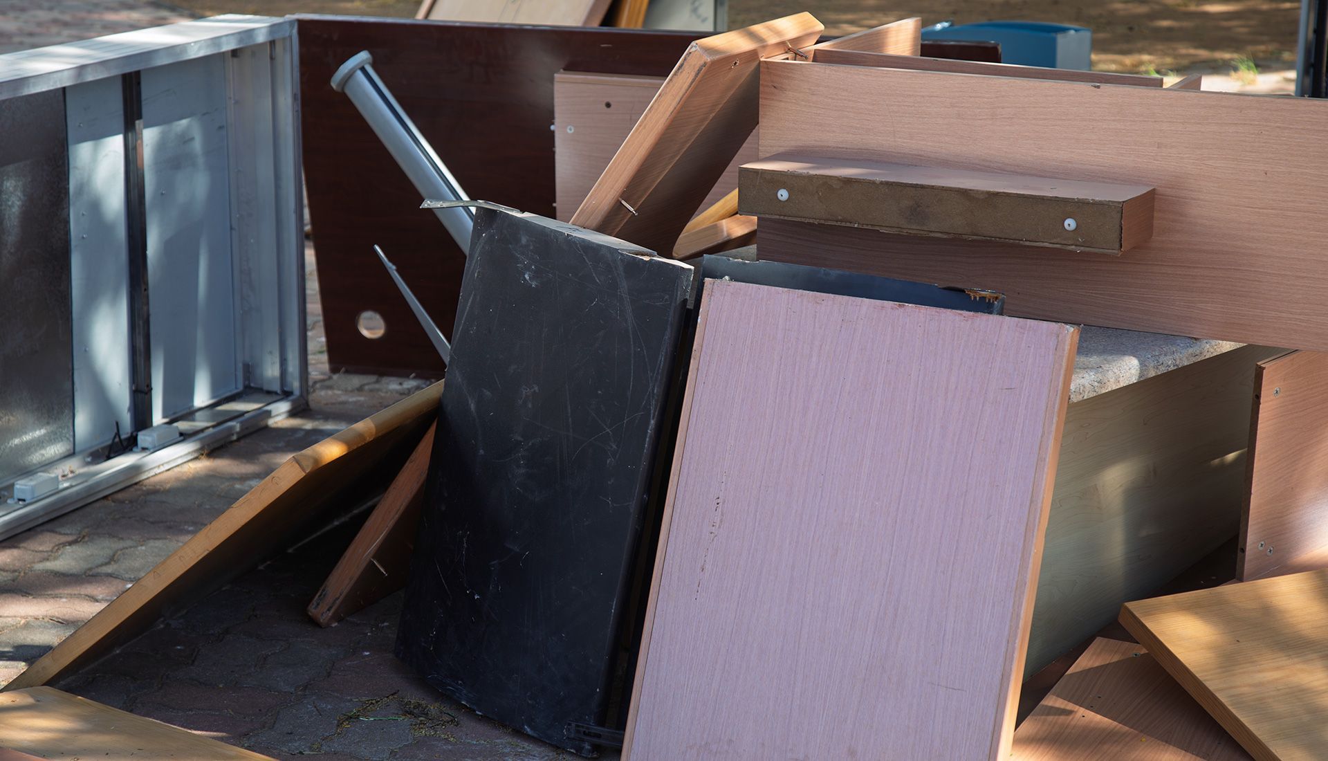 Garbage truck collecting green bins on a narrow city street. Workers in safety vests. Buildings with shops line the street.