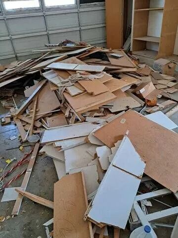 Pile of wood debris and scattered materials inside a room with shelves and a window.