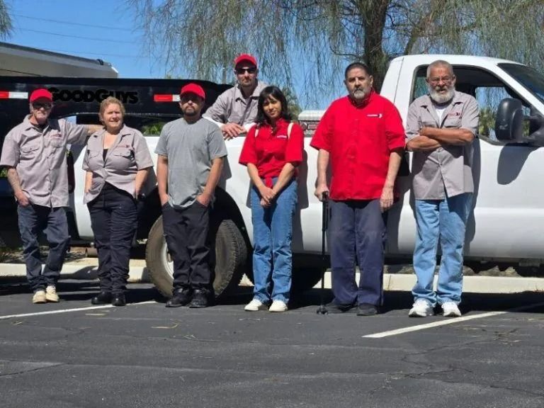Group of people in work uniforms standing in front of a white truck. Some wearing red shirts, others gray.