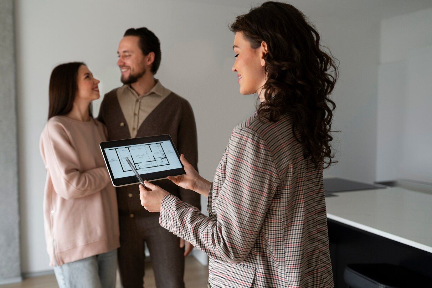 Real estate agent showing a couple a floor plan on a tablet in an empty room.