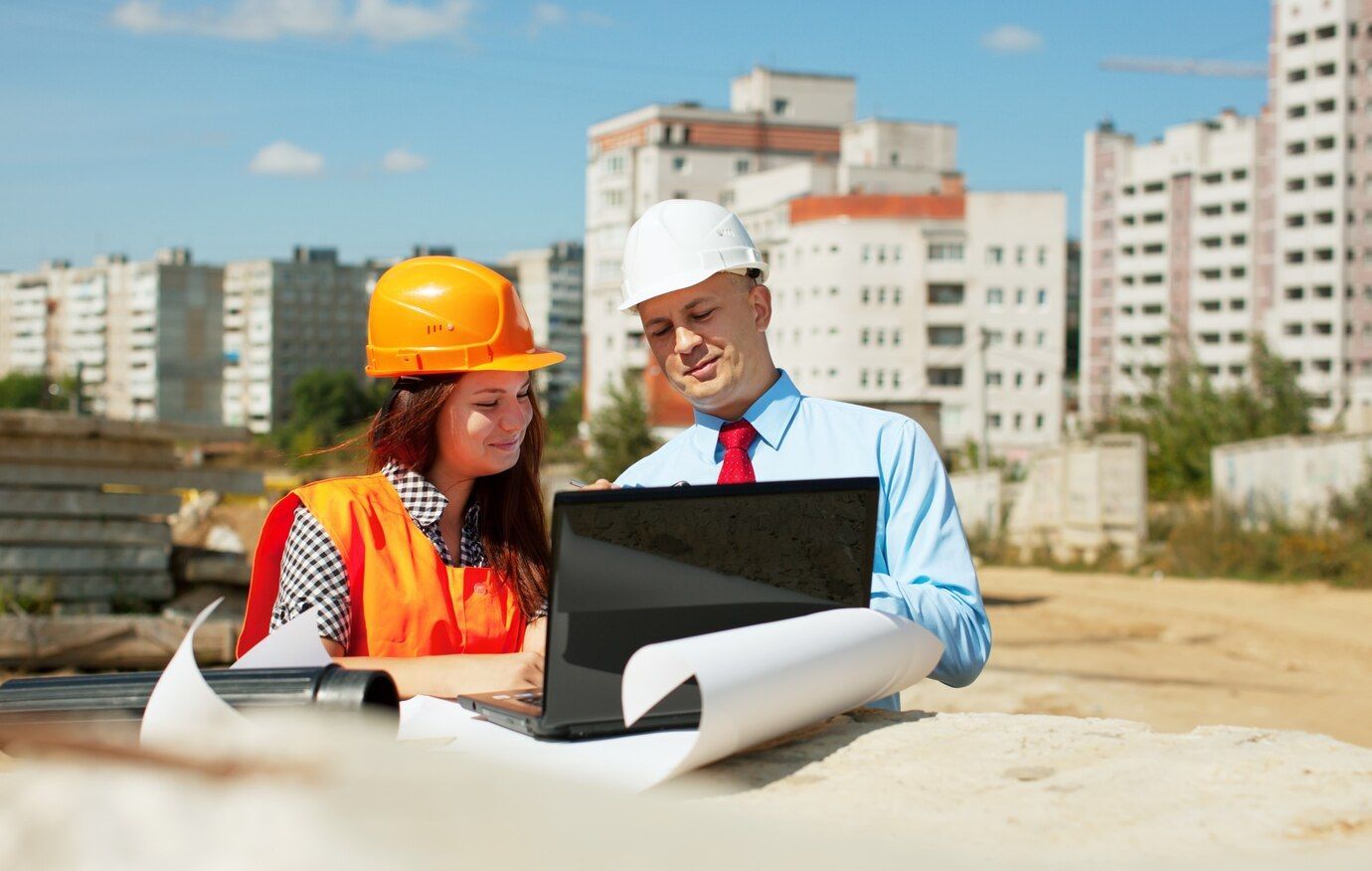 Construction workers reviewing plans and laptop on site.