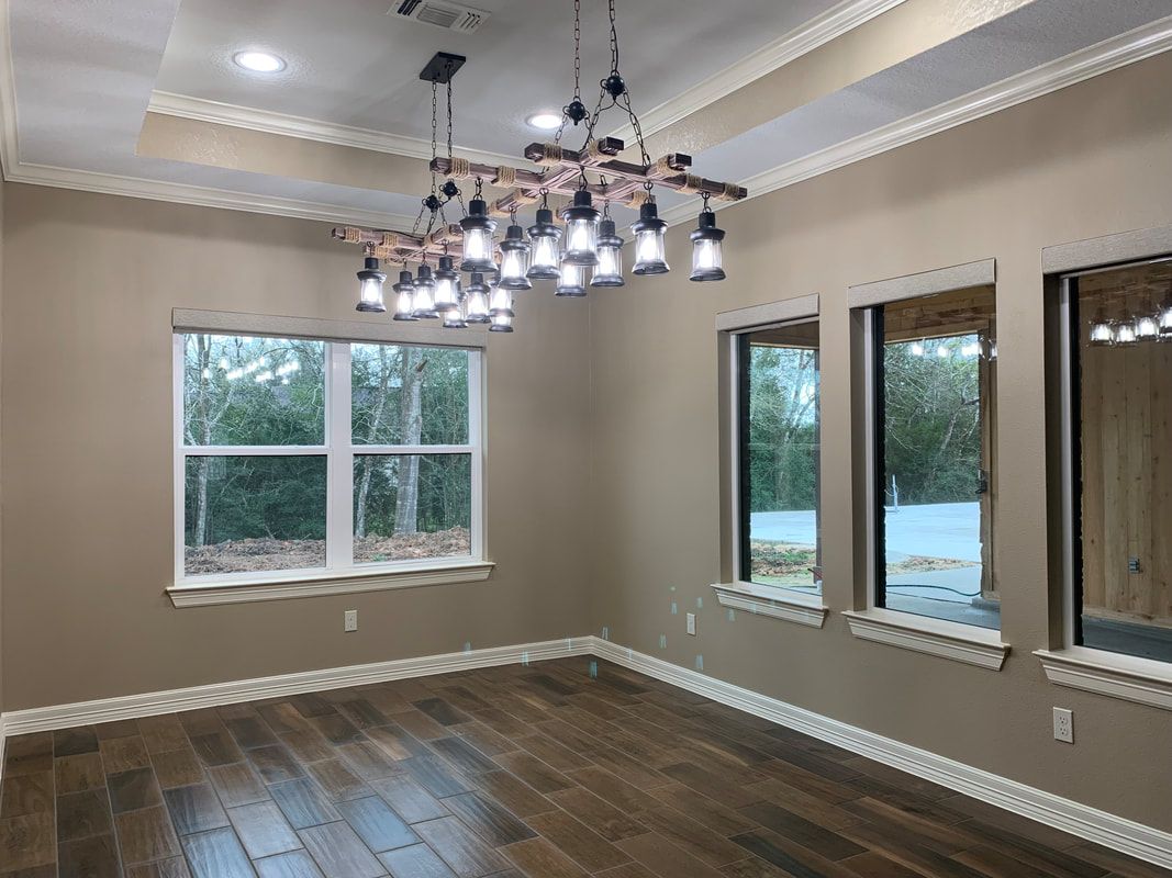 Empty room with wood floors, brown walls, and large windows.  A unique chandelier hangs from the ceiling.