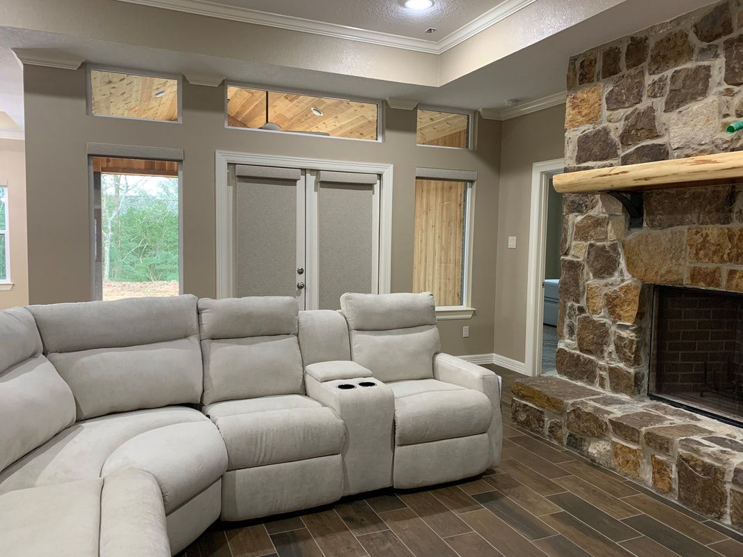 Living room with white sectional sofa, stone fireplace, and boarded up windows.