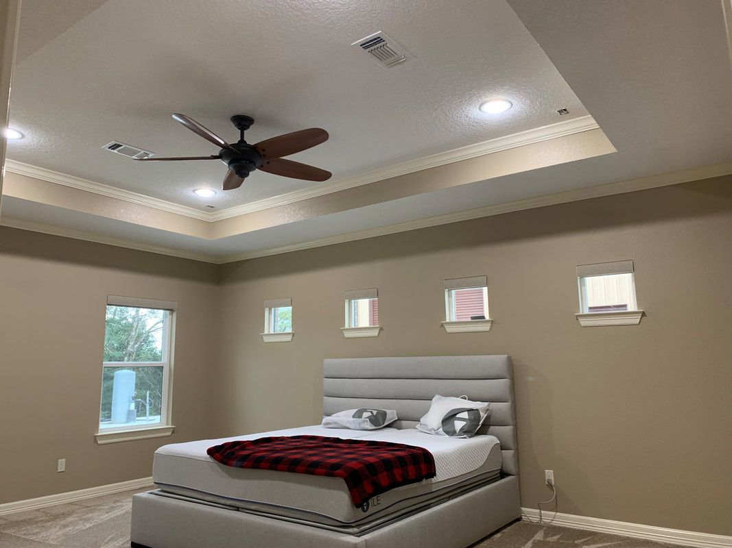 Bedroom with a bed, small windows, and a ceiling fan. Beige walls and a tray ceiling.