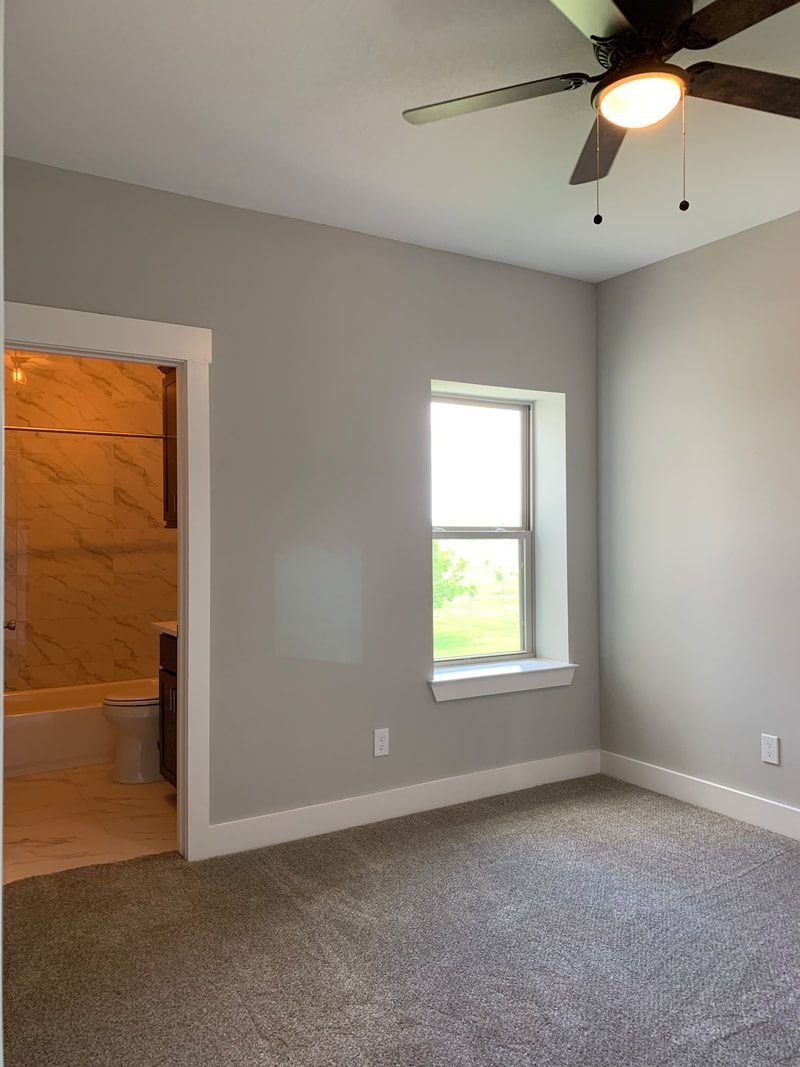 Bedroom with gray walls, window, and door to bathroom. Ceiling fan with light.