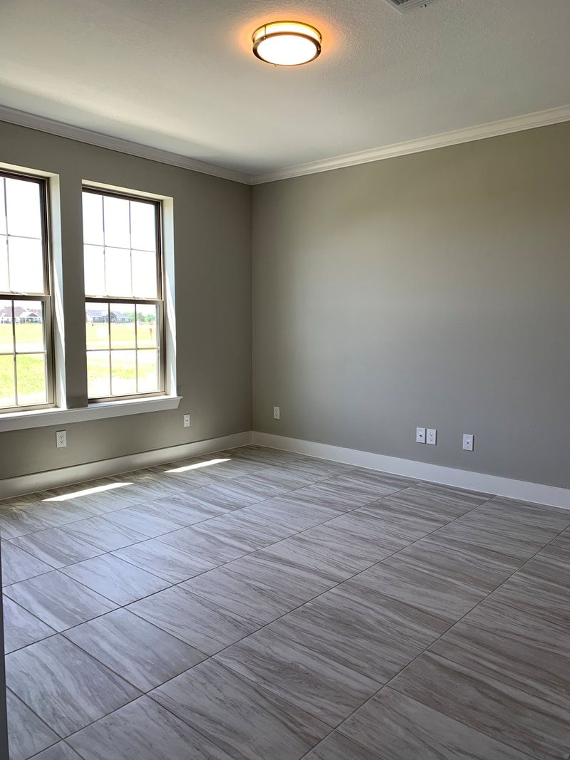 Empty room with gray walls, two windows, and light tile flooring. Ceiling light fixture.