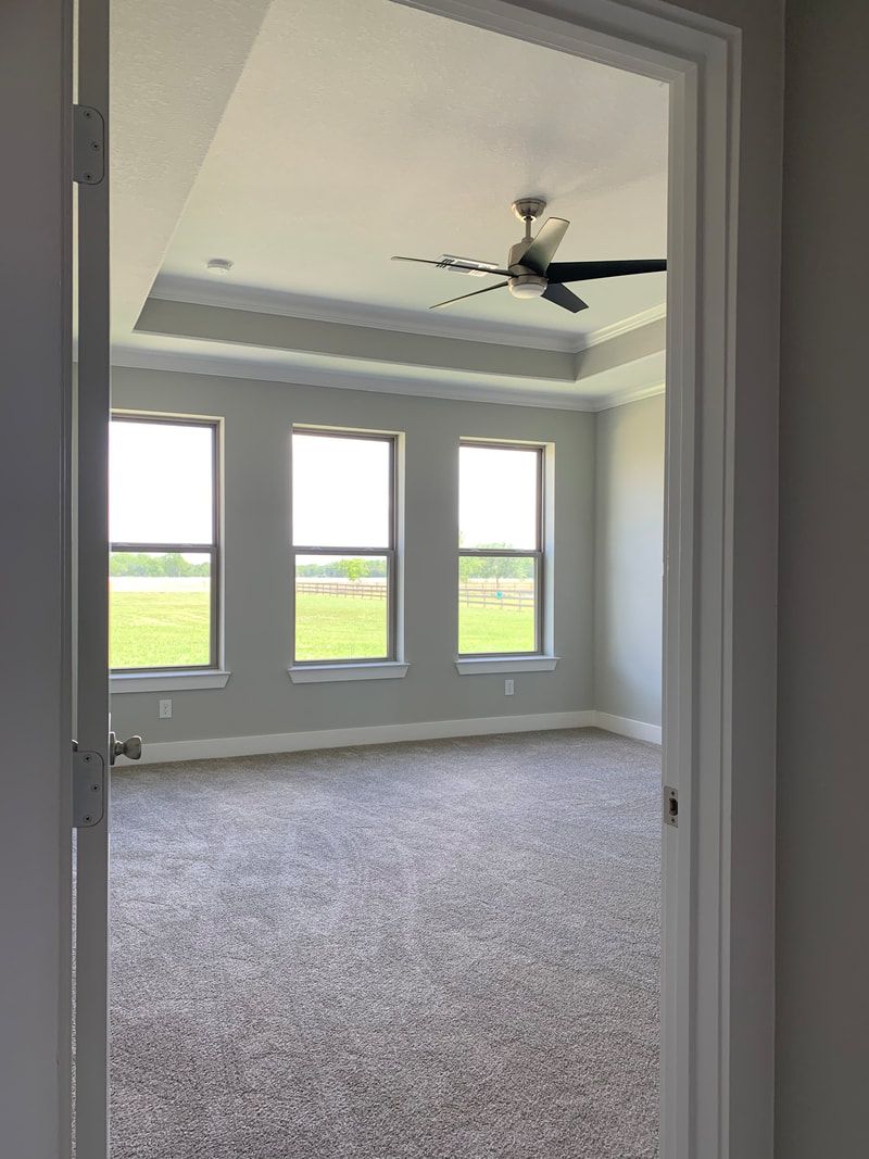 View of an empty bedroom through an open doorway, windows, ceiling fan, and carpeted floor.