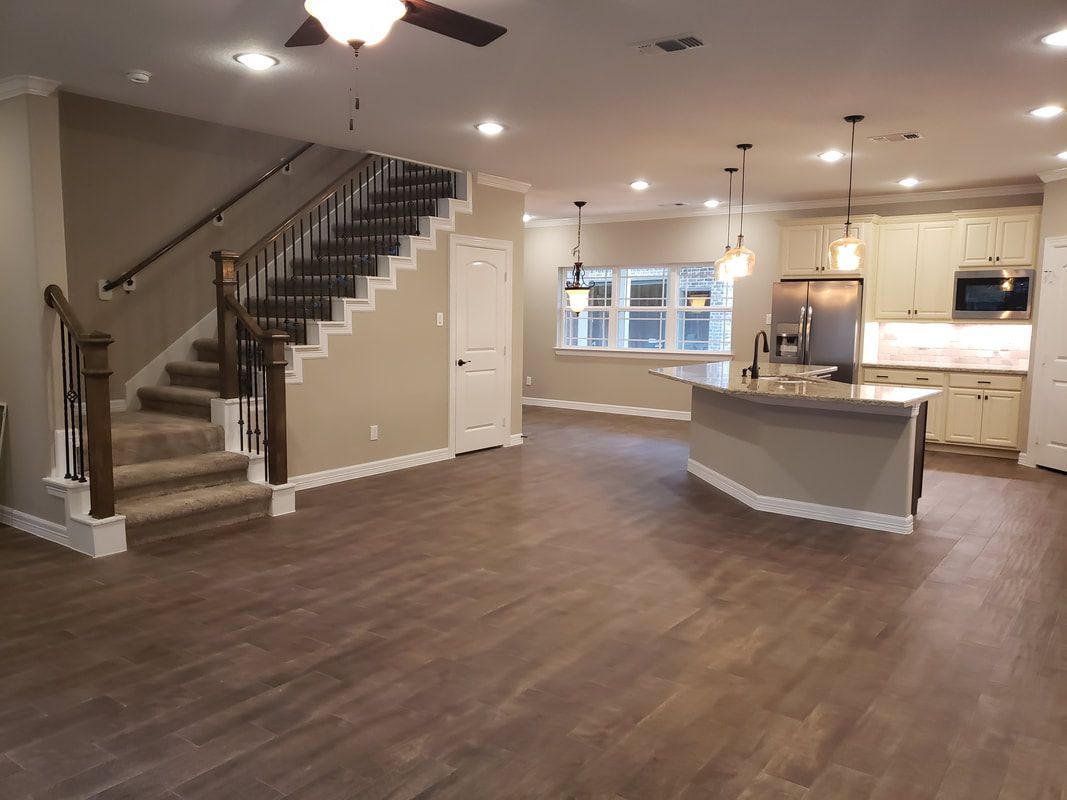 Open-concept home interior with staircase, kitchen island, and wood-look flooring. Neutral tones throughout.