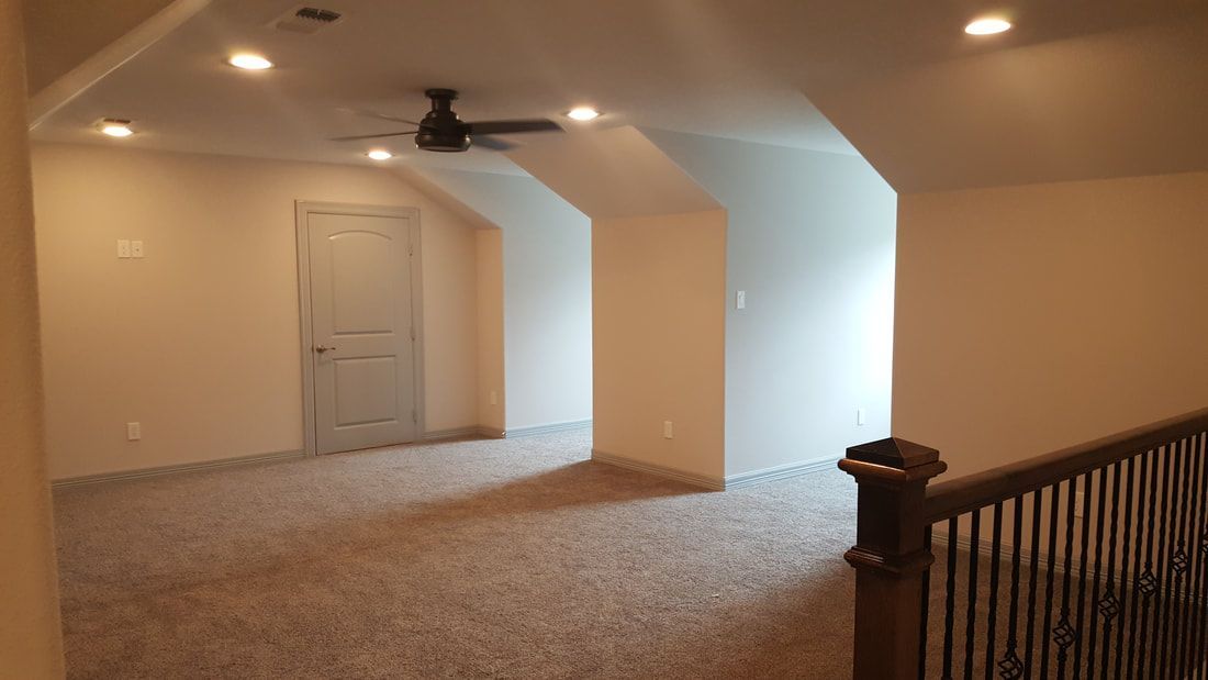 A carpeted room with a door, angled walls, and a ceiling fan; a railing is in the foreground.