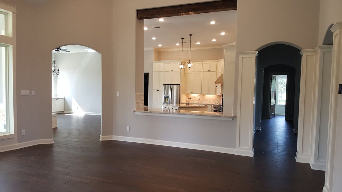 Interior of a home with arched doorways, dark wood floors, and a kitchen visible through an opening.