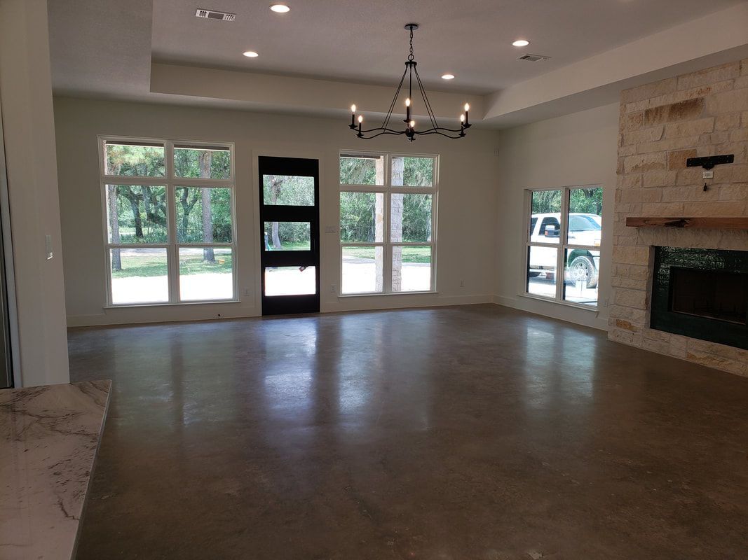 Spacious, empty room with large windows, fireplace, dark door, and polished concrete floor.