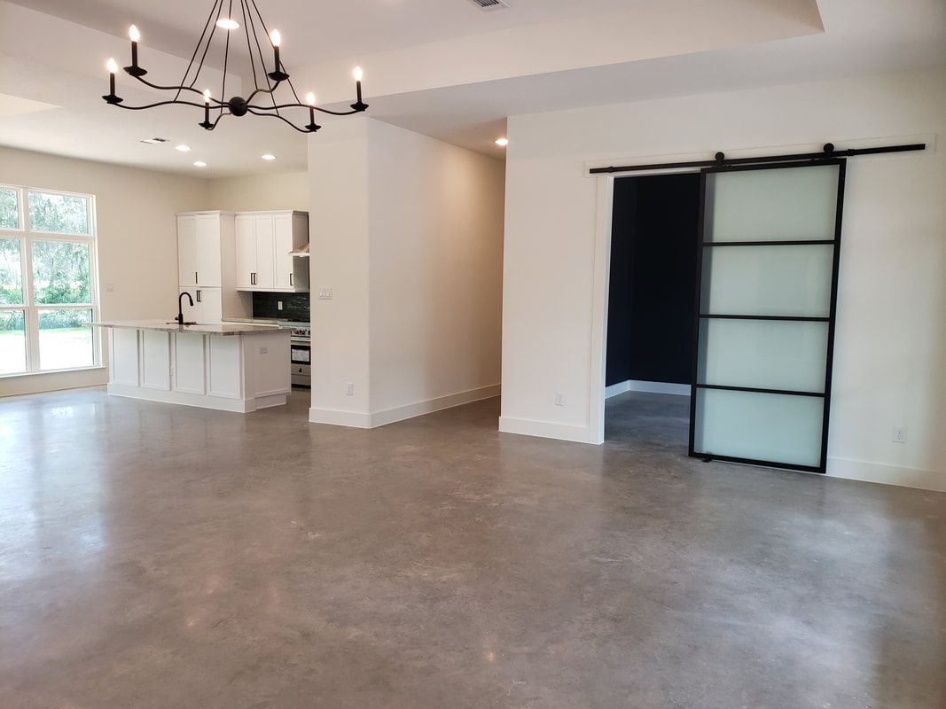 Open-plan living space with kitchen and sliding glass-paneled door; concrete floor and white walls.